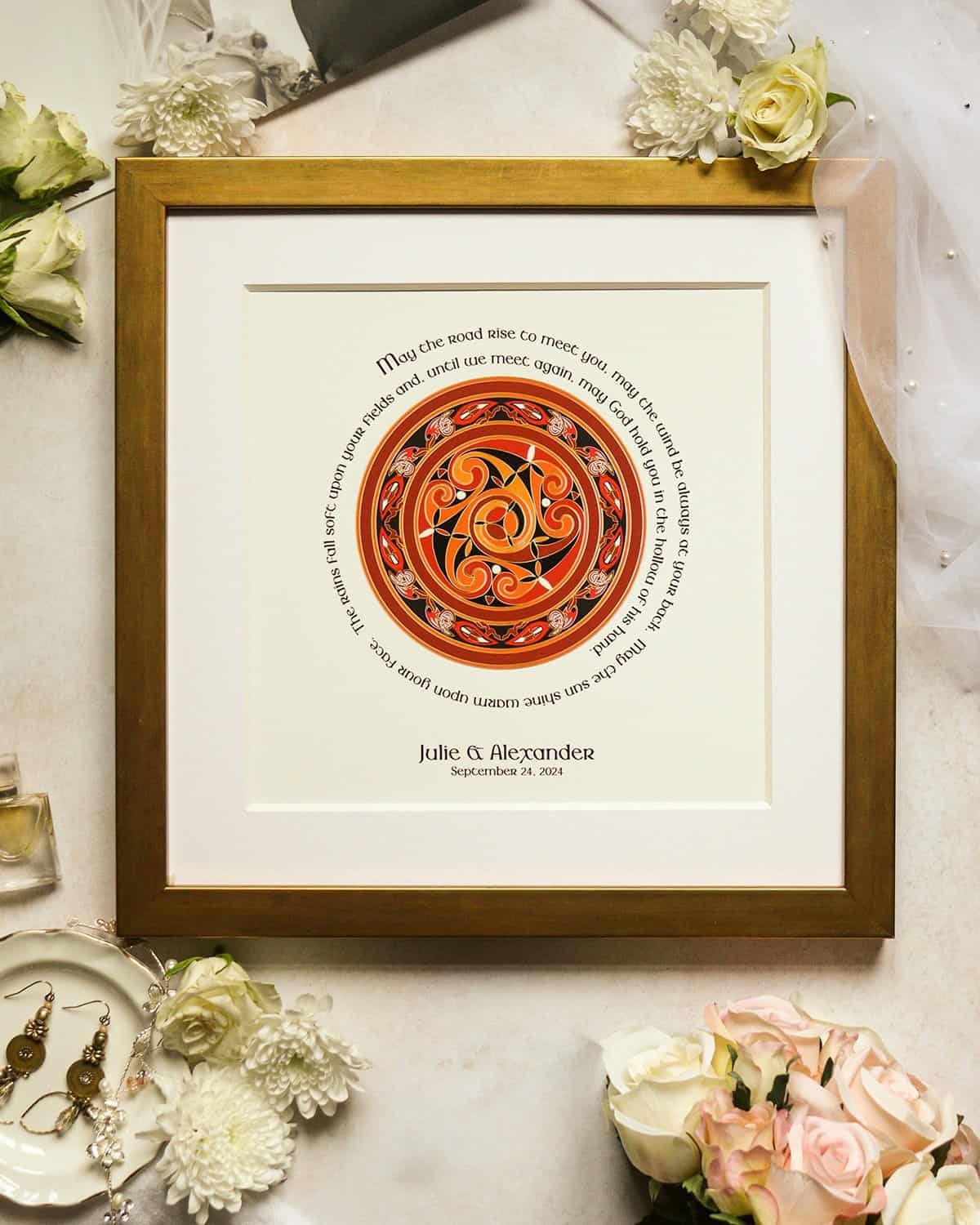 Framed Irish wedding blessing print with intricate Celtic knotwork in red and gold, featuring a heartfelt blessing in elegant script. The couple’s names and wedding date add a personal touch. Surrounded by white roses, pearls, and vintage gold earrings, this sentimental keepsake makes a perfect Irish wedding gift.